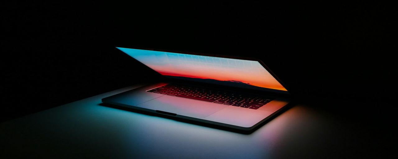 A laptop glowing on a desk in a dark room