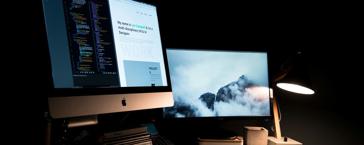 Two monitors on a desk showing code and a design