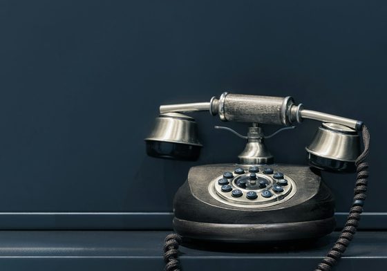 Telefon klasik di atas meja berlatarkan dinding hijau kebiruan gelap