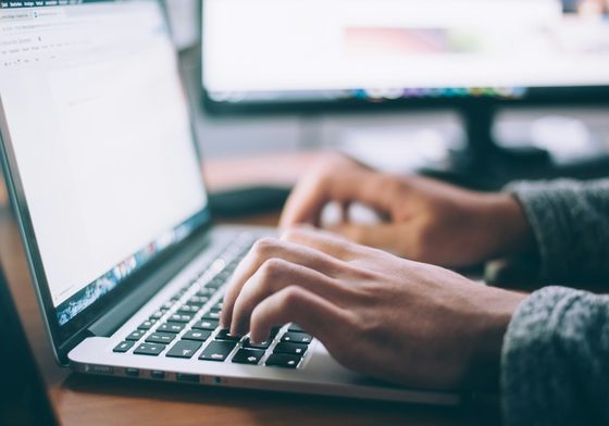 Hands typing a domain name into a laptop