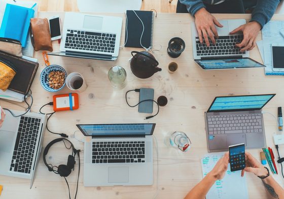 Pasukan merancang projek laman web di meja yang penuh komputer riba dan nota